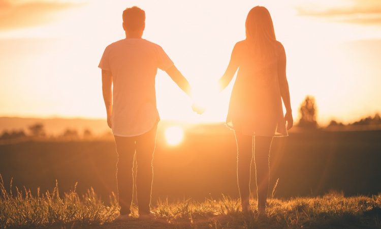 Par gåendes hand i hand på åker i solnedgång