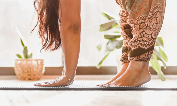 Händer och fötter av en kvinna som står nerböjd på en yogamatta.